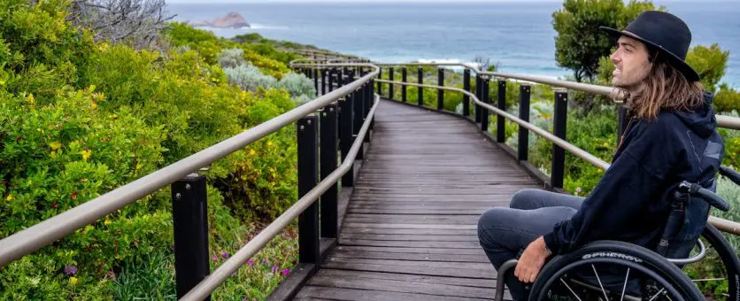 Man wearing hat in wheelchair takes a breather on the accessible wooden track on the Cape to Cape walk